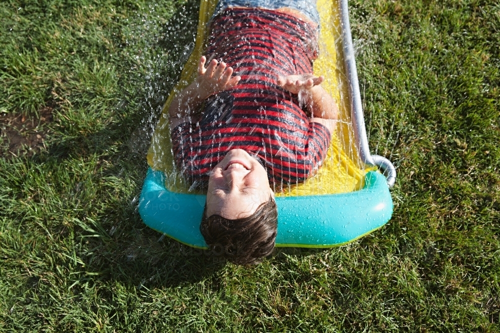 Happy tween boy lying in a sprinkler on a hot summer's day - Australian Stock Image