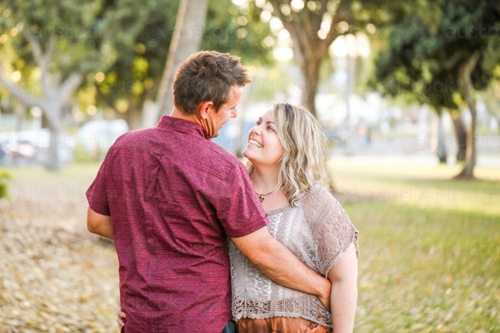 Happy twenty-something couple embracing in golden afternoon light at the park - Australian Stock Image