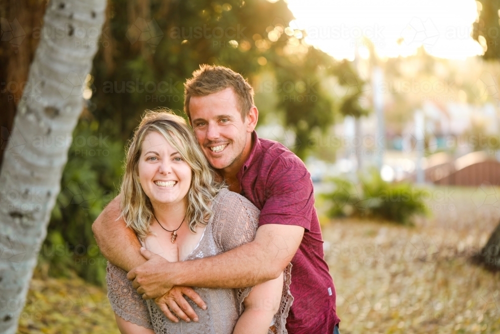 Happy twenty-something couple embracing in golden afternoon light at the park - Australian Stock Image