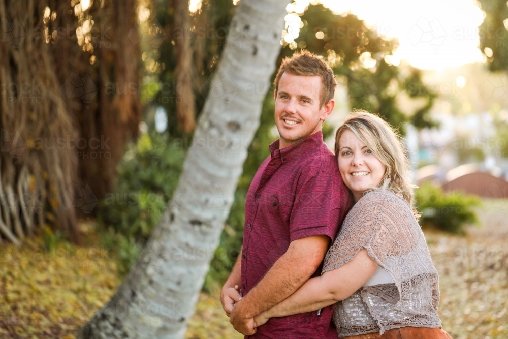 Happy twenty-something couple embracing in golden afternoon light at the park - Australian Stock Image