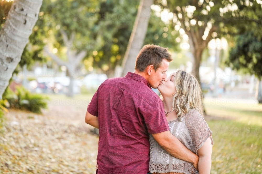 Happy twenty-something couple embracing in golden afternoon light at the park - Australian Stock Image