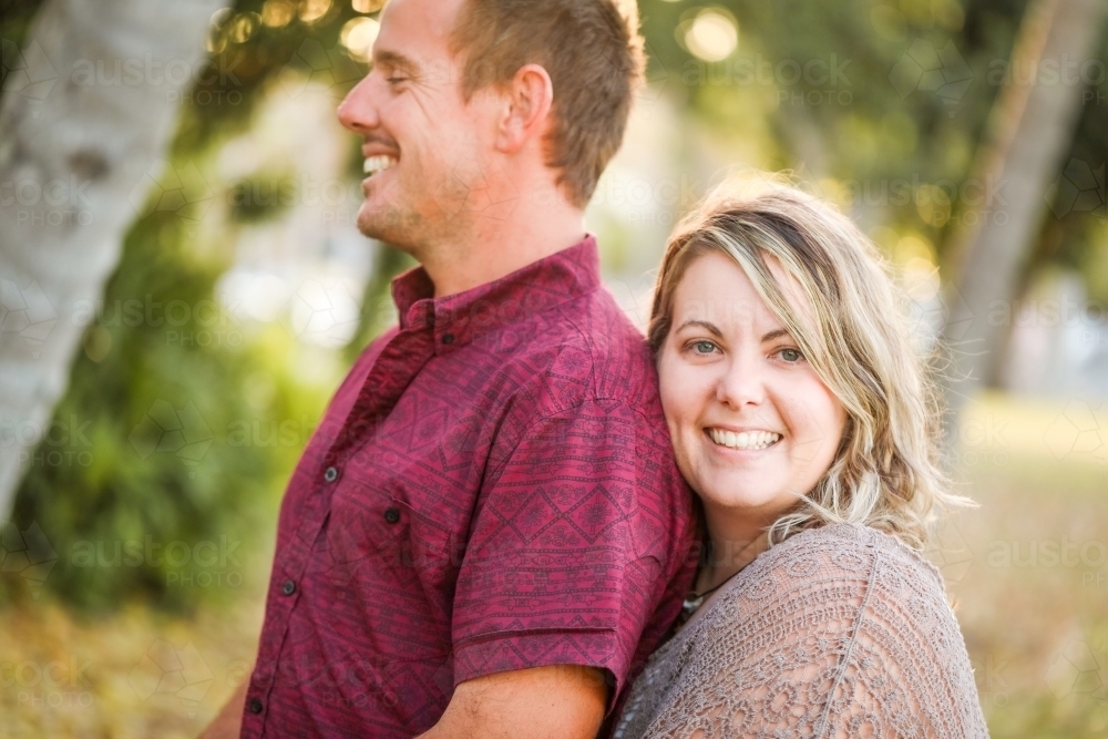 Happy twenty-something couple embracing in golden afternoon light at the park - Australian Stock Image