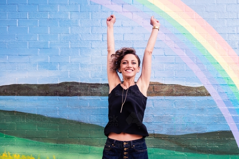 happy woman in front of brick wall with rainbow mural - Australian Stock Image