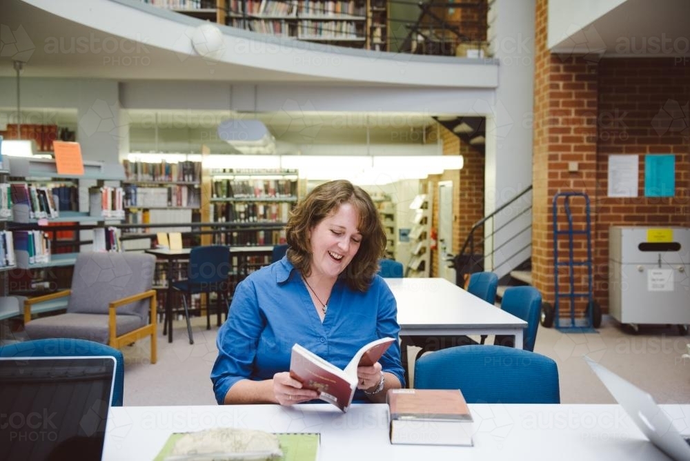 Happy woman reading a book in the university library - Australian Stock Image