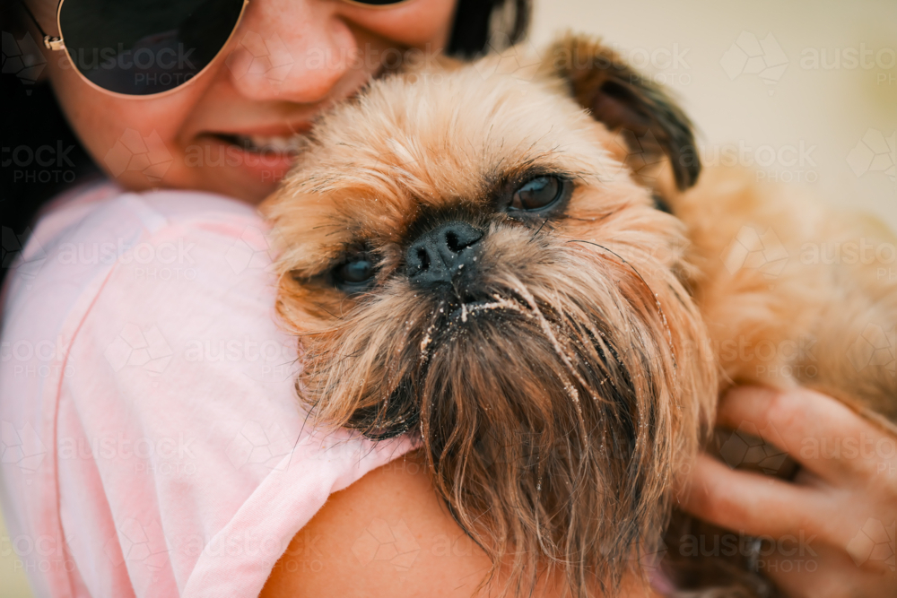 Happy woman snuggling Brussels Griffon dog at the beach - Australian Stock Image