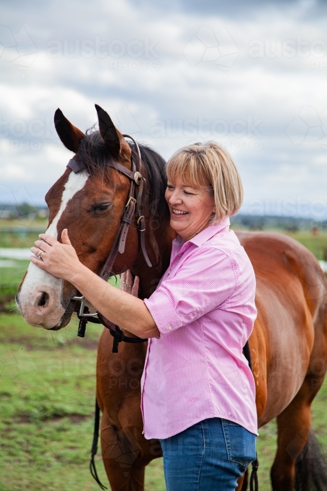 Happy woman standing at her horses head holding bridle - Australian Stock Image