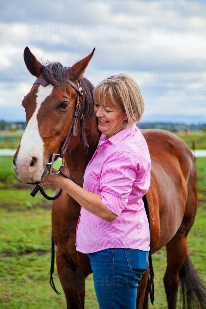 Happy woman standing at her horses head holding bridle - Australian Stock Image