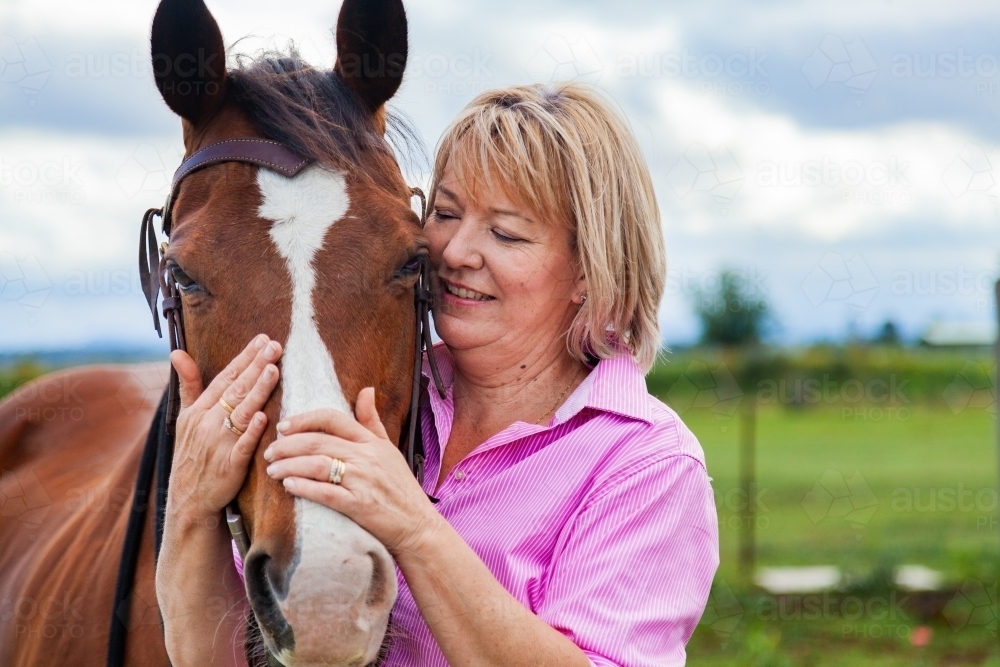 Happy woman standing at her horses head holding bridle - Australian Stock Image