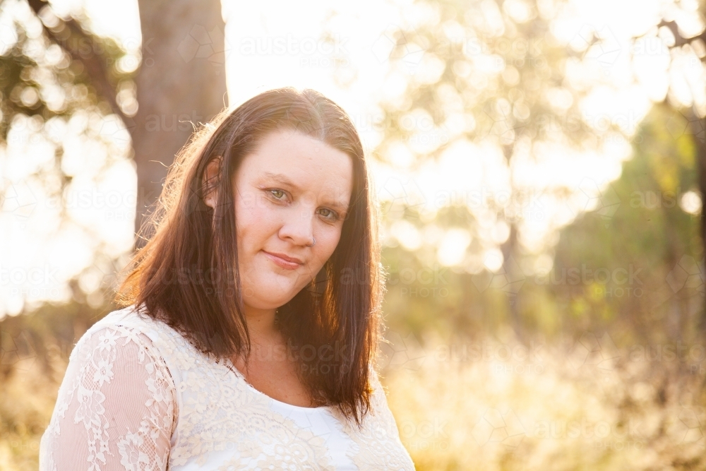 Happy woman standing in bushland in warm golden light - Australian Stock Image
