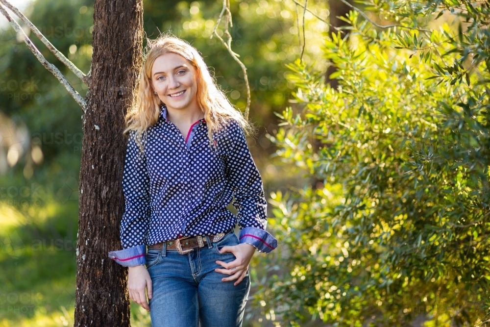 Happy young adult person standing against a tree outside - Australian Stock Image
