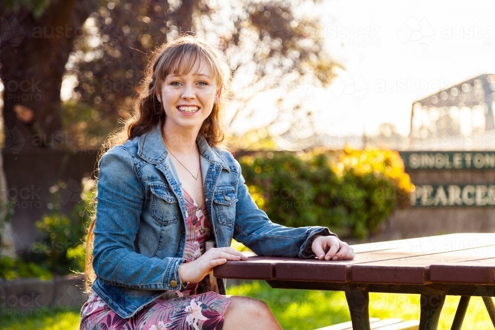 Happy young adult sitting at park bench in autumn - Australian Stock Image
