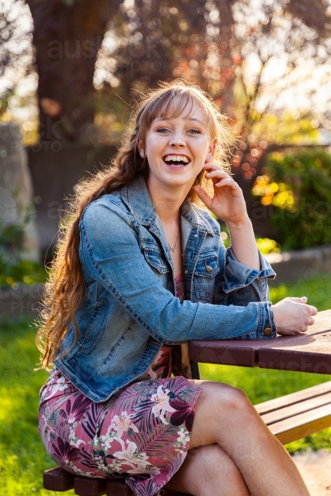 Happy young adult sitting at park bench in autumn - Australian Stock Image