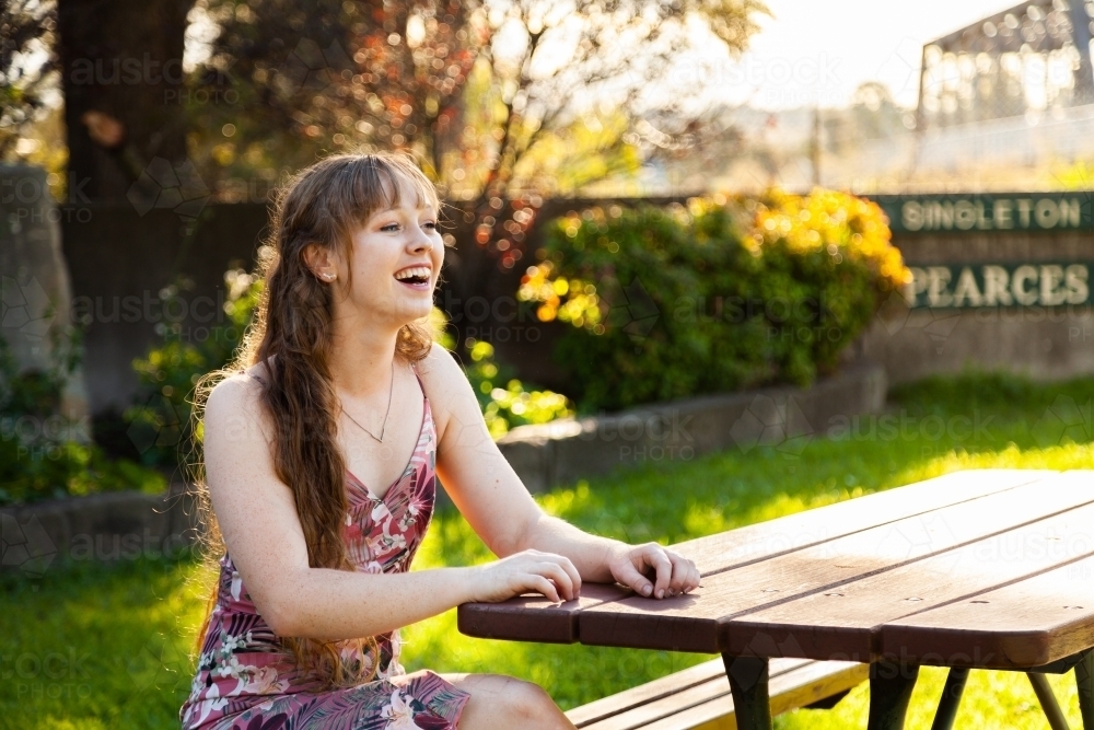 Happy young adult sitting at park bench in autumn - Australian Stock Image