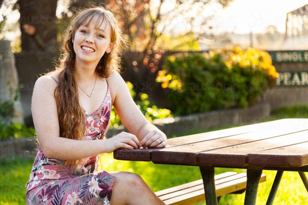 Happy young adult sitting at park bench in autumn - Australian Stock Image