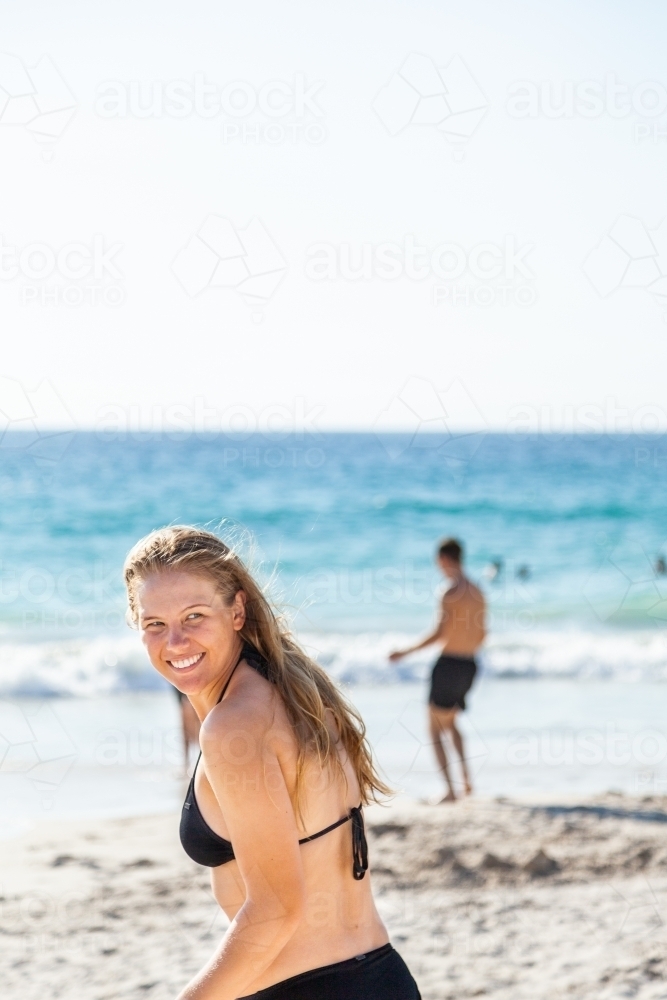 Happy young adult woman looking over her shoulder as she runs down to the sea at the beach - Australian Stock Image
