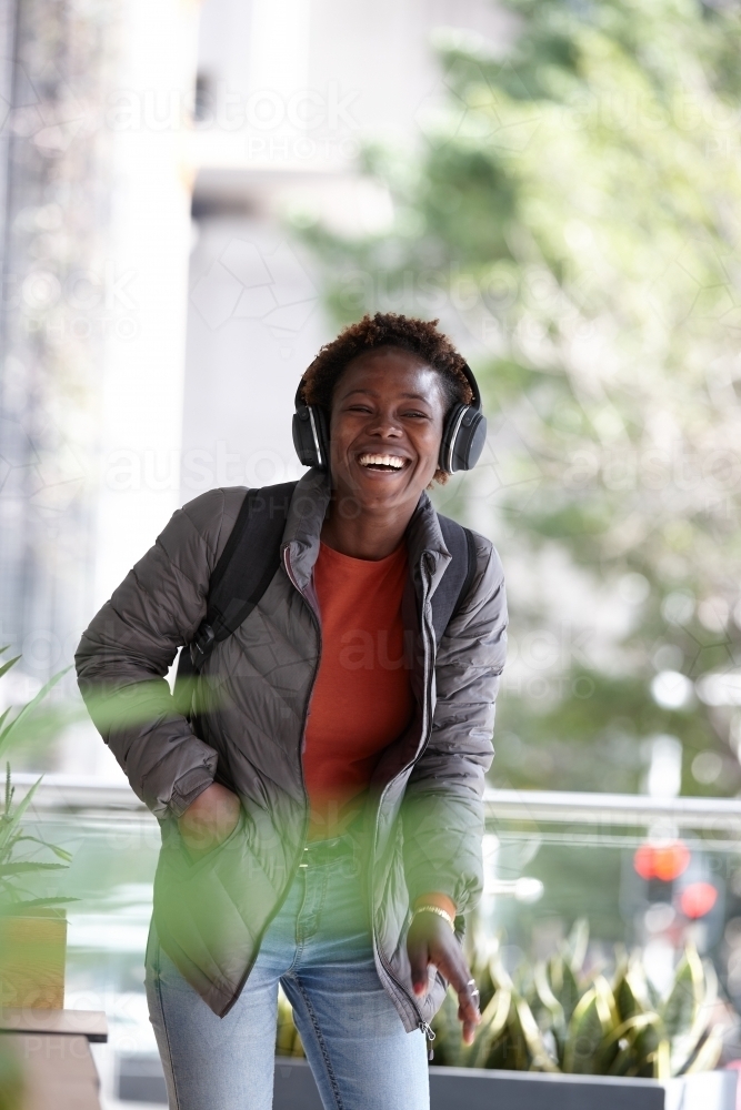 Happy young African woman listening to music wearing wireless headphones in city - Australian Stock Image