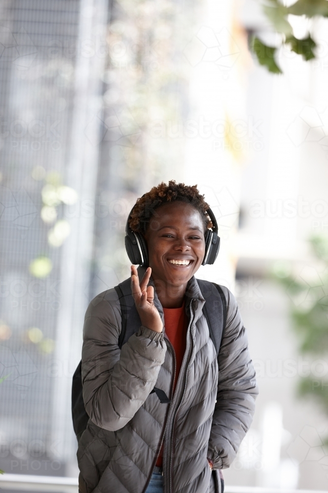 Happy young African woman listening to music wearing wireless headphones in city - Australian Stock Image
