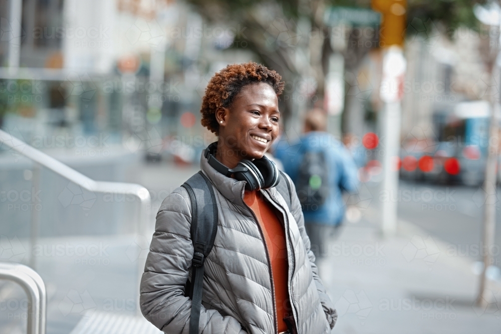 Happy young African woman wearing wireless headphones in city - Australian Stock Image