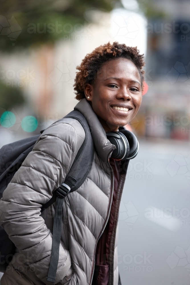Happy young African woman wearing wireless headphones in city - Australian Stock Image
