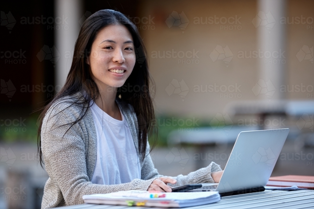 happy Young Asian university student studying on laptop outdoors - Australian Stock Image