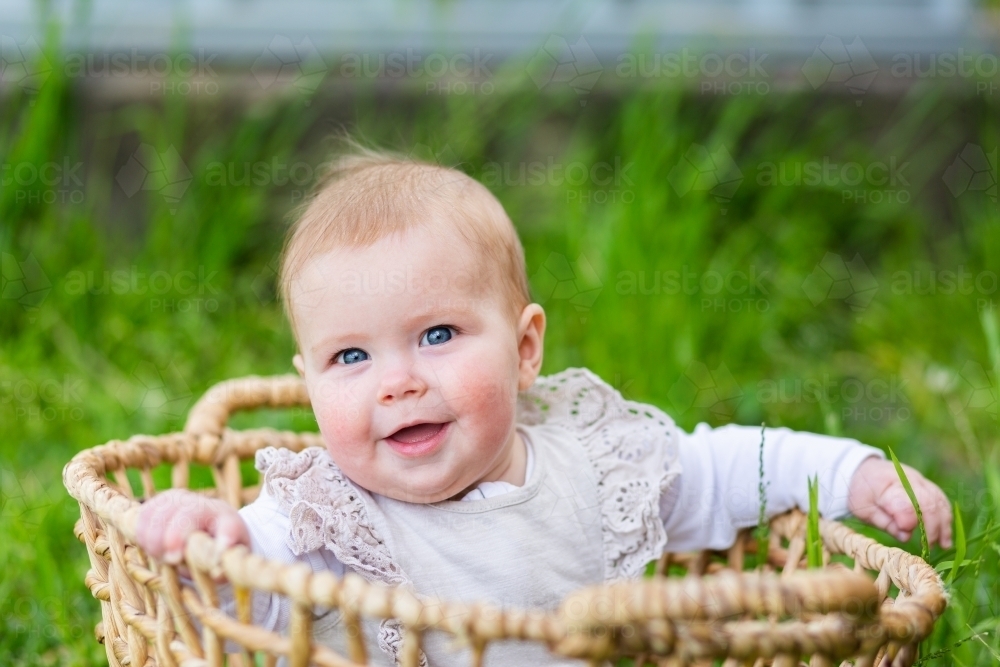 Image of Happy young baby sitting up in washing basket outside smiling