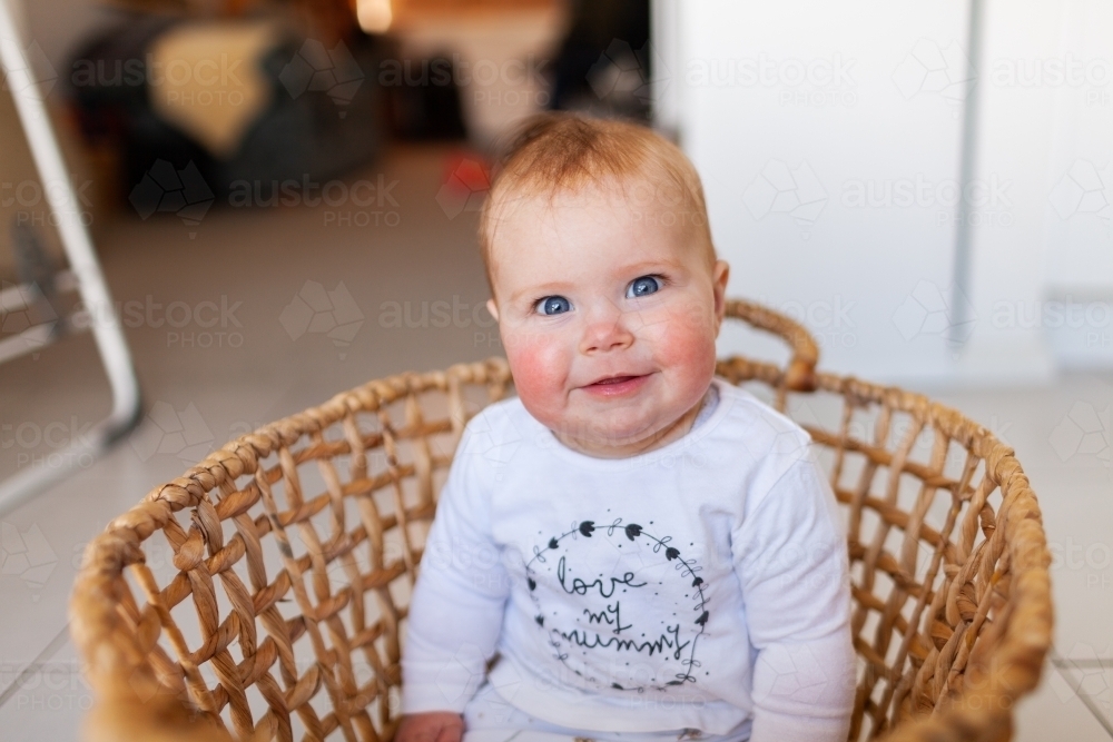 Happy young baby sitting up in washing basket with shirt saying love my mummy - Australian Stock Image