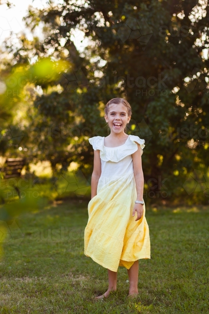 Happy young barefoot girl in park spinning around in yellow dress - Australian Stock Image