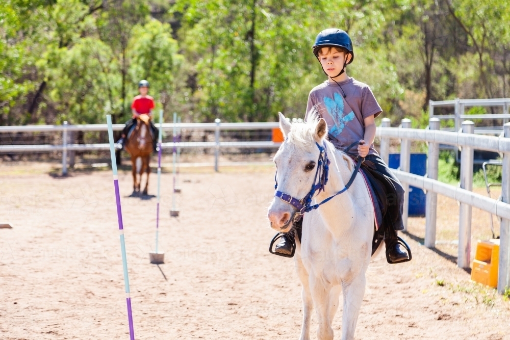 Happy young boy on white pony getting riding lessons - active kids - Australian Stock Image
