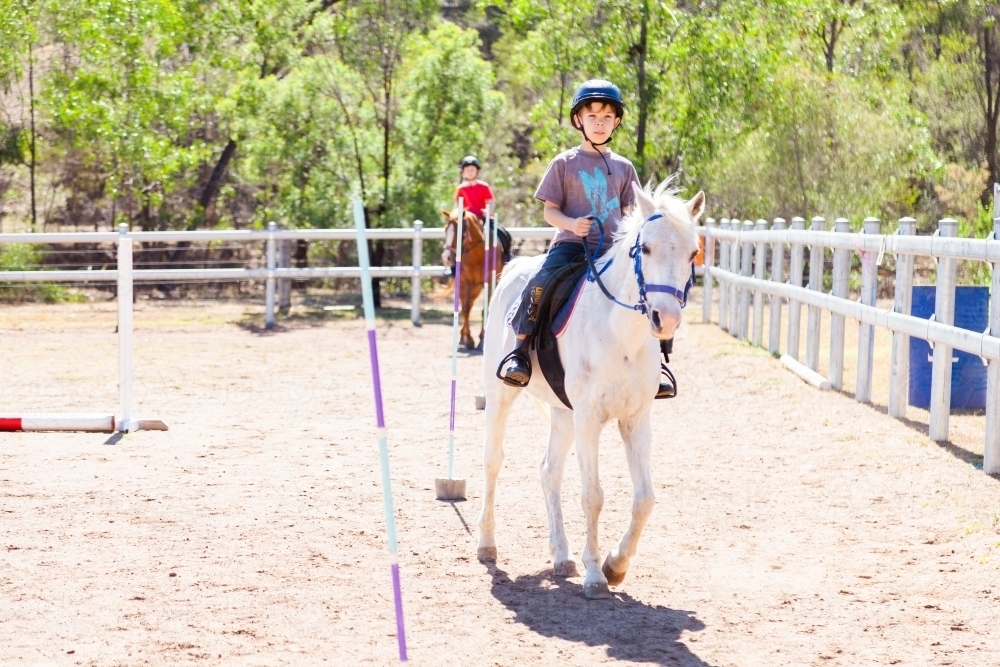 Happy young boy on white pony getting riding lessons - active kids - Australian Stock Image