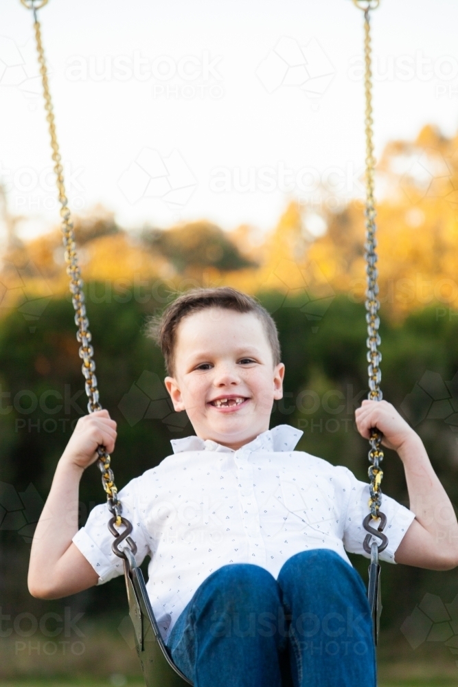 Happy young boy playing on a swing at a park - Australian Stock Image