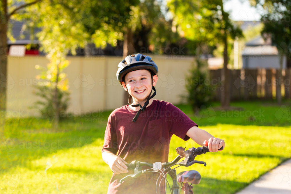 happy young boy with big smile looking to the side while holding bike at park - Australian Stock Image