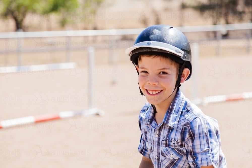 Happy young boy with safety horse riding helmet on horseback during lesson - Australian Stock Image