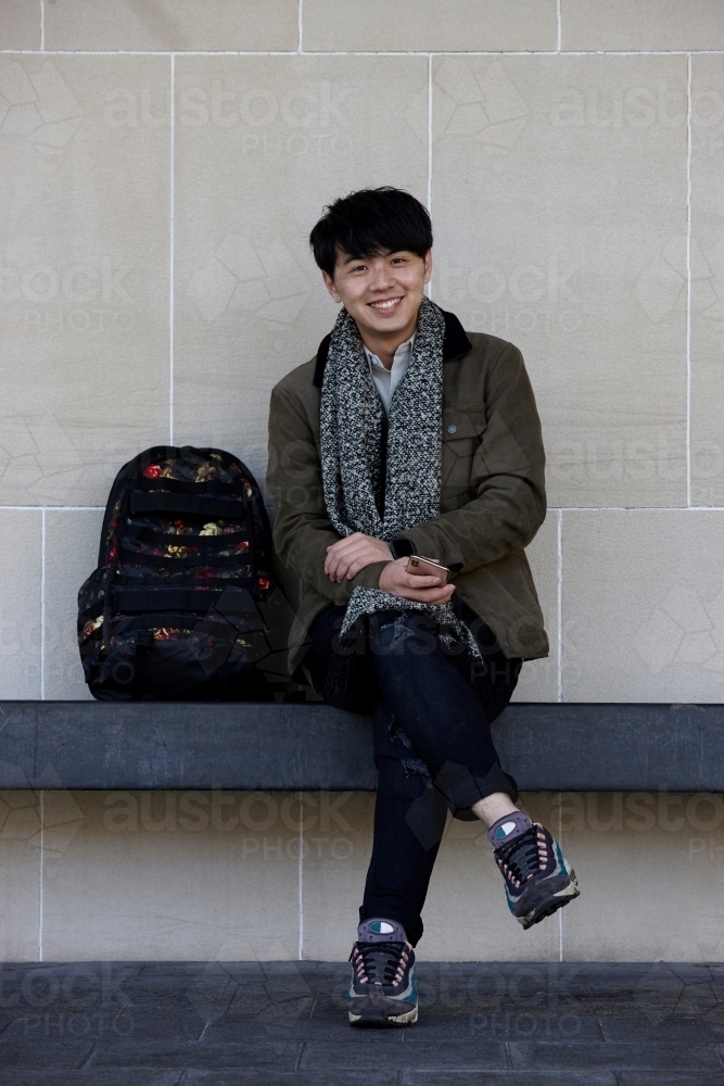 Happy young Chinese man seated holding mobile phone - Australian Stock Image