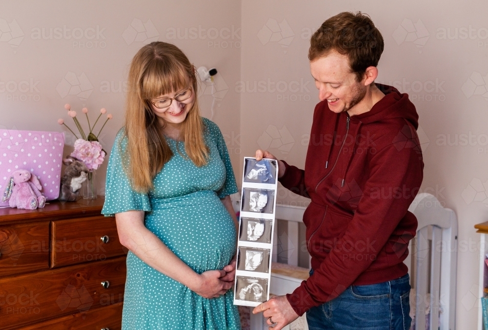 Happy young couple in their twenties holding ultrasound picture strip of baby - Australian Stock Image