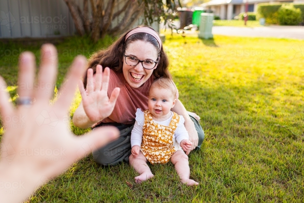Happy young family laugh and high five on lawn outside home - Australian Stock Image