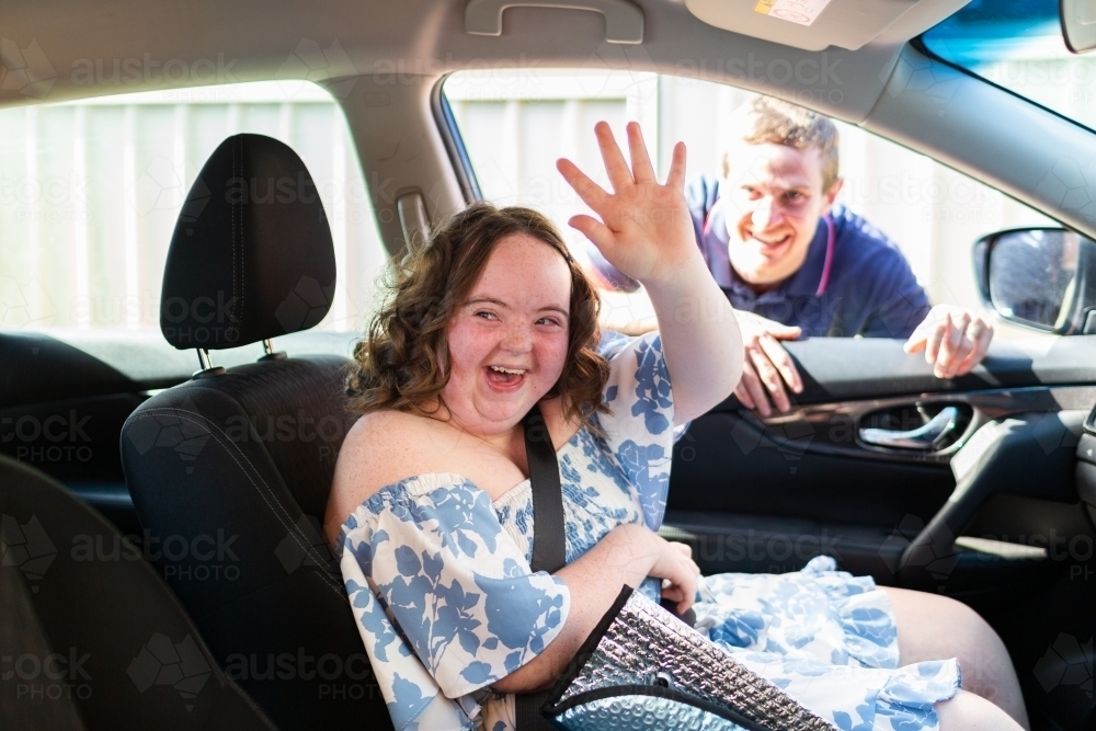 Happy young female person with down syndrome in car passenger seat waving goodbye - Australian Stock Image