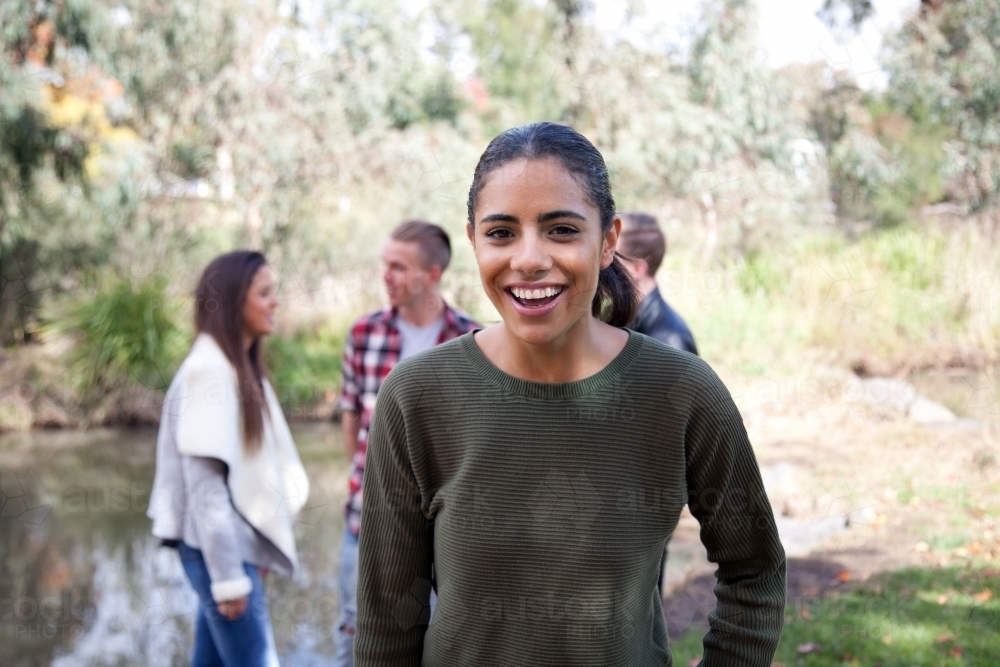 Happy young female standing in front of group of friends in outdoor setting - Australian Stock Image