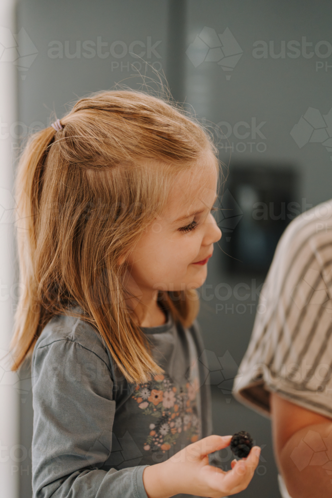 Happy young girl eating blackberry in the kitchen. - Australian Stock Image