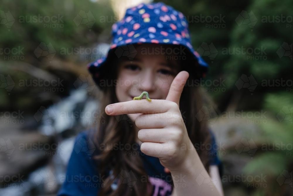 Happy young girl in a rainforest with a green caterpillar crawling on her finger - Australian Stock Image