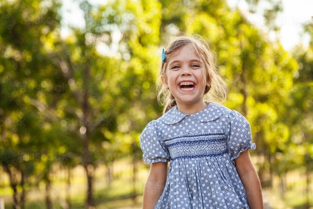 Happy young girl laughing outside wearing dress - Australian Stock Image