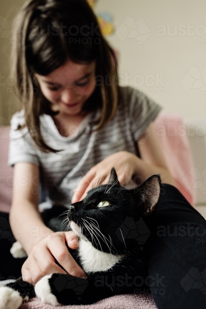 Happy young girl sitting on her bed with her black and white cat. - Australian Stock Image