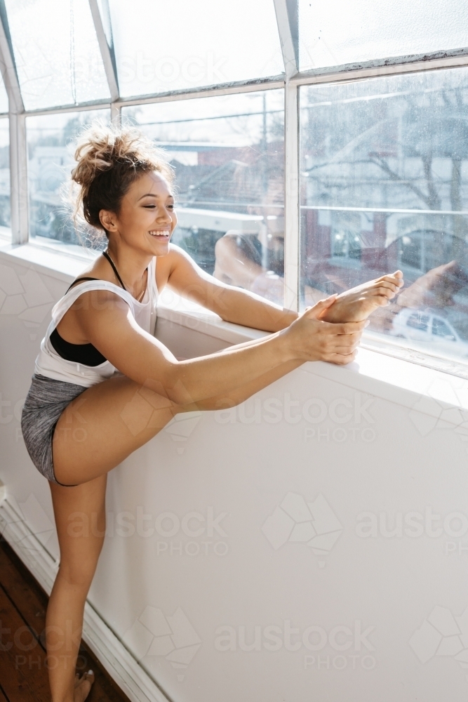 Happy young girl stretching before a dance class at a window - Australian Stock Image