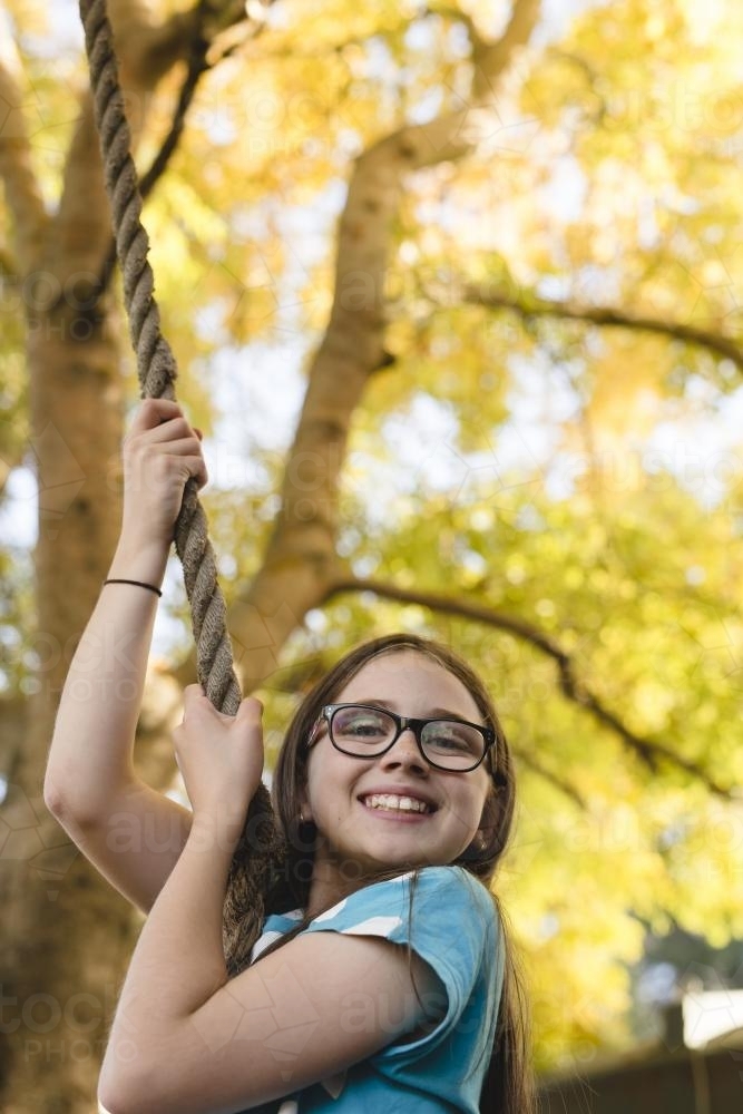 Happy young girl swinging on a rope swing in backyard - Australian Stock Image