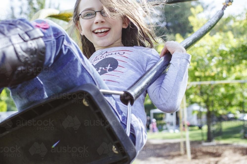 Happy young girl swinging on swing - Australian Stock Image