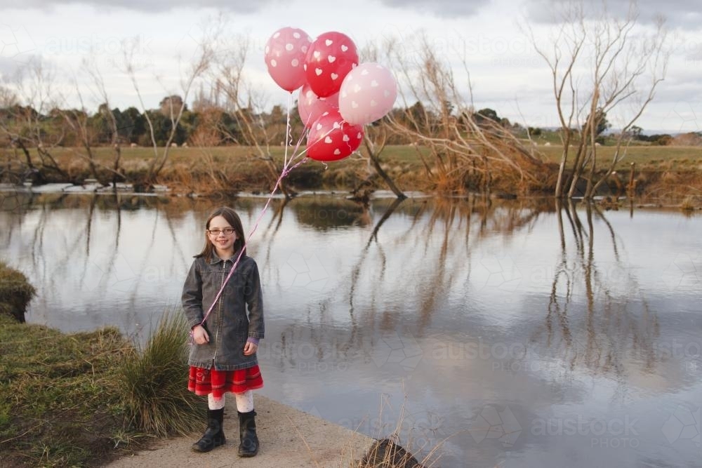 Happy young girl with a bunch of birthday pink balloons beside a river - Australian Stock Image