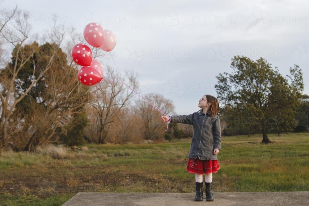 Happy young girl with a bunch of pink balloons outside - Australian Stock Image