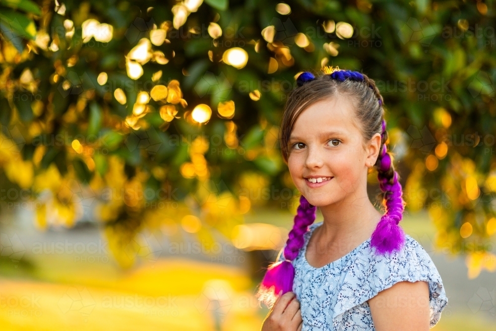 Happy young girl with fun purple braids in hair smiling in warm golden light with copy space - Australian Stock Image