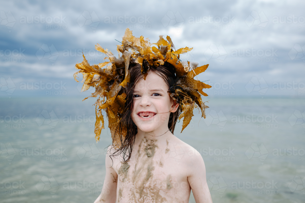 Happy young girl with two missing front teeth at the beach wearing a crown of seaweed looking scary - Australian Stock Image