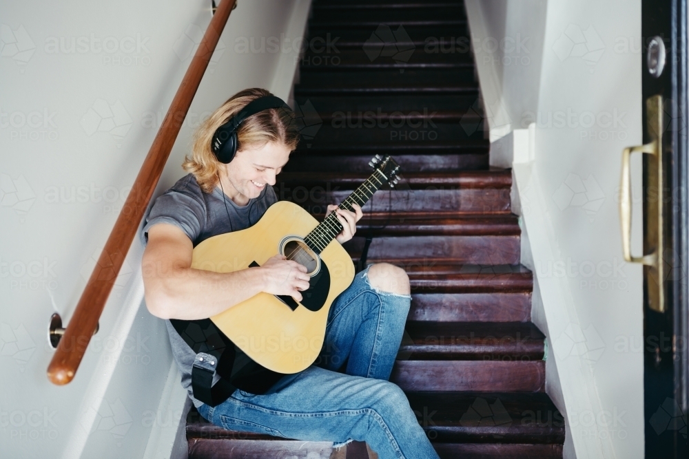 Happy young guy playing his guitar with headphones - Australian Stock Image