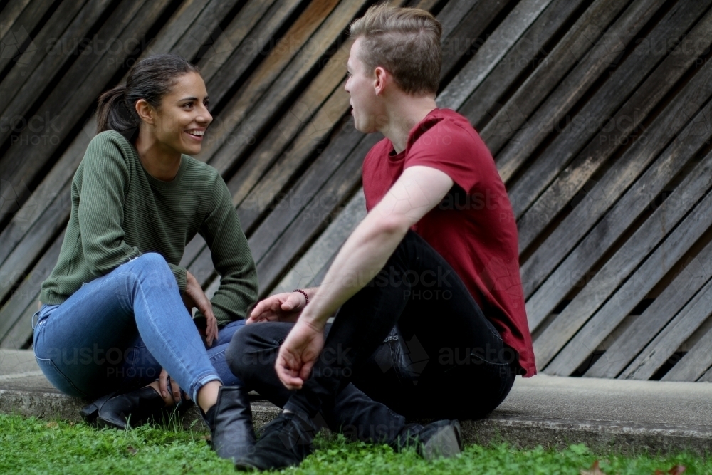 Happy young interracial couple sitting on the ground and chatting - Australian Stock Image